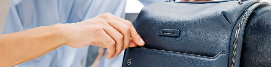 Hand opening the front pocket of a blue leather Piquadro backpack
